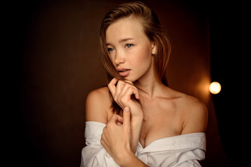 beautiful woman with brunette hair and blue eyes in white shirt posing on dark background in studio