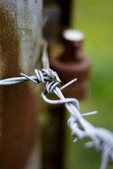 Barbed wired fence secured to rusty metal post providing security to farmland in rural Hampshire with shallow depth of field