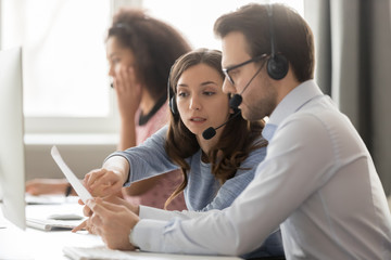 Call center agents in headsets discussing papers helping at workplace