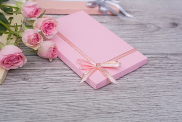 Hands holding craft paper pink gift boxes with as a present for Christmas, new year, valentine day, mothers day and womans day or anniversary on wooden background decorated with roses.