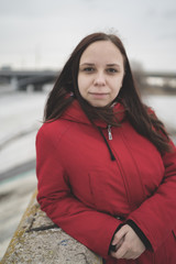 Obraz premium Beautiful girl in a red jacket on the pier in the spring posing against the water. Woman on the waterfront