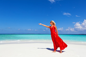 Beautiful , blonde woman in a red dress with  arm raised at Maldives beach.Copy space