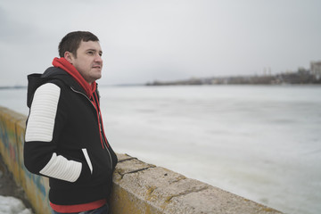 Handsome guy in a jacket on the dock in the spring of posing on the background of the water. The man on the waterfront