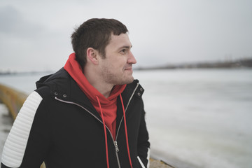 Handsome guy in a jacket on the dock in the spring of posing on the background of the water. The man on the waterfront