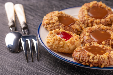 Shortbread cookies made of walnut dough with strawberry jam and caramel on a plate with a fork and spoon.