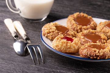 Shortbread cookies made of walnut dough with strawberry jam and caramel on a plate with a fork and spoon. Glass of milk.