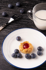 Shortbread cookies made of walnut dough with strawberry jam on a plate with blueberries and a fork.