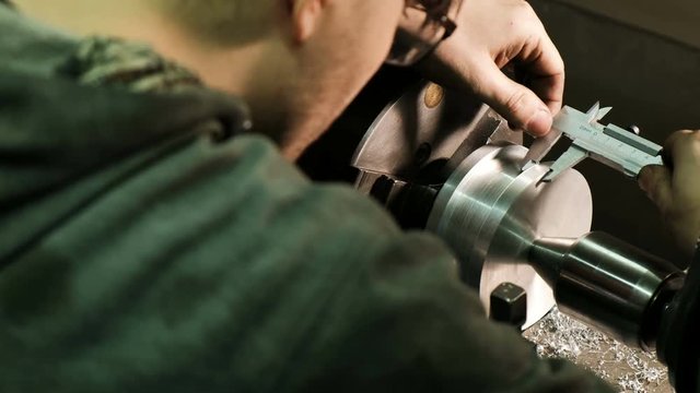 Turner measures the dimensions of the metal workpiece with a caliper. Work on a lathe