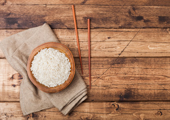 Wooden bowl with boiled organic basmati jasmine rice and wooden chopsticks with linen towel on old wooden background.Space for text