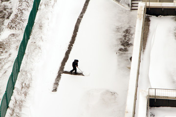 Janitor cleans the kindergarten yard after a snowfall. View from above.