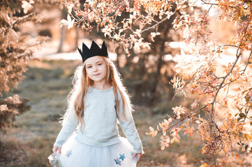 Stylish baby girl wearing princess dress and handmade black crown outdoors. Looking at camera. Spring season.