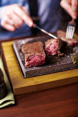 sirloin steak on a very hot stone being cooked by a man to his own taste on a wooden table with a knife and fork