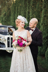 Happy newlywed couple, man and wife kissing near stylish retro car