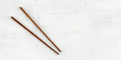 Flat lay photo - pair of dark wood chopsticks on white board. Wide banner for asian / chinese food, space for text on right.