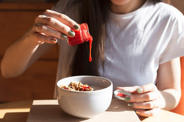 A young beautiful woman came to the cozy cafe in the morning to eat breakfast with a delicious granola sitting at a table near a large bright window