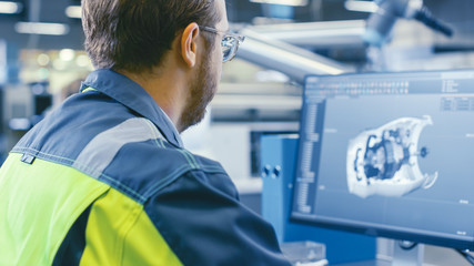 Back Shot of an Mechanical Engineer Working on Computers, Designing in 3D Model of the Engine using CAD Software. At the Factory.