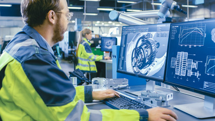 At the Factory: Mechanical Engineer Works on Computer, Designs in CAD 3D Model of the Engine. In...