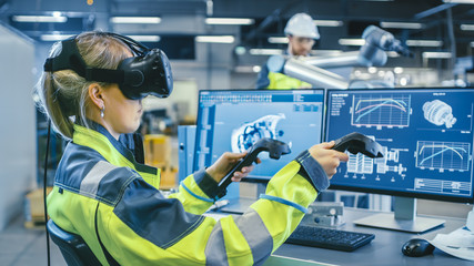 Factory: Female Industrial Engineer Wearing Virtual Reality Headset and Holding Controllers, She...