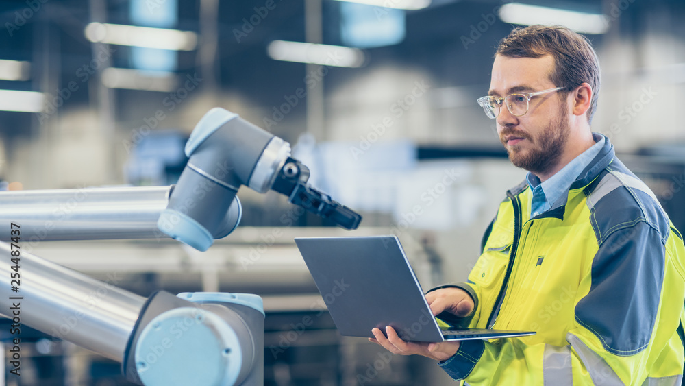 Poster At the Factory: Automation Engineer Uses Laptop for Programming Robotic Arm. New Era in Automatic Manufacturing Industry.