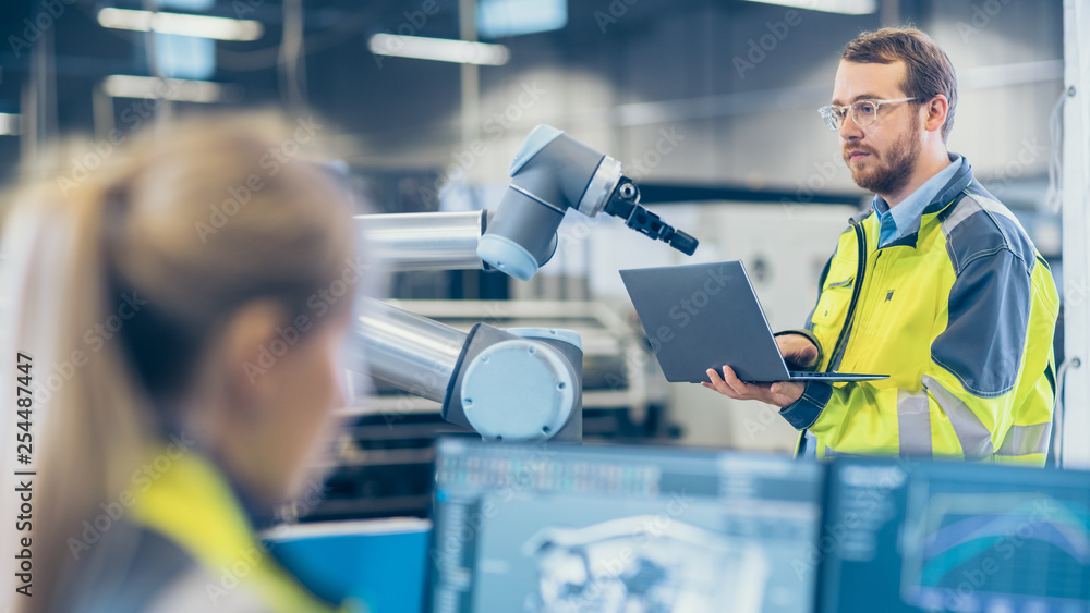 Poster At the Factory: Female Mechanical Engineer Designs 3D Engine on Her Personal Computer, Male Automation Engineer Uses Laptop for Programming Robotic Arm.