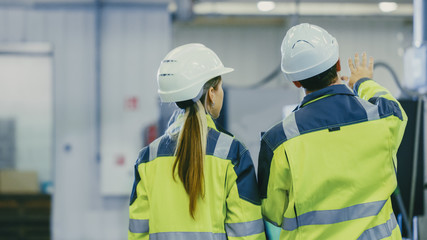 Male Industrial Worker and Female Chief Mechanical Engineer in Walk Through Manufacturing Plant...