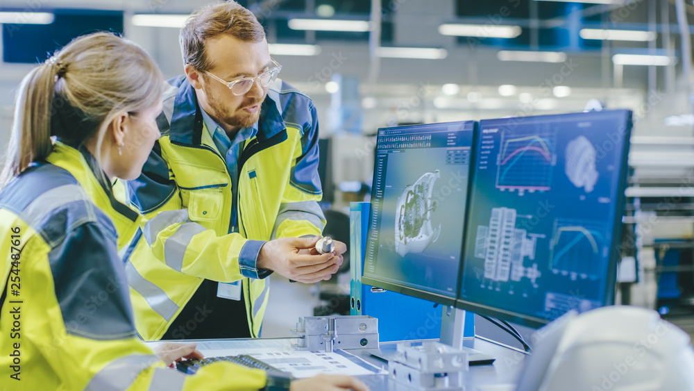 Poster At the Factory: Male Mechanical Engineer Holds Component and Female Chief Engineer Work on Personal Computer, They Discuss Details of the 3D Engine Model Design for Robotic Arm.