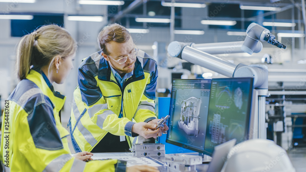 Poster At the Factory: Male Mechanical Engineer Holds Component and Female Chief Engineer Work on Personal Computer, They Discuss Details of the 3D Engine Model for Robotic Arm.