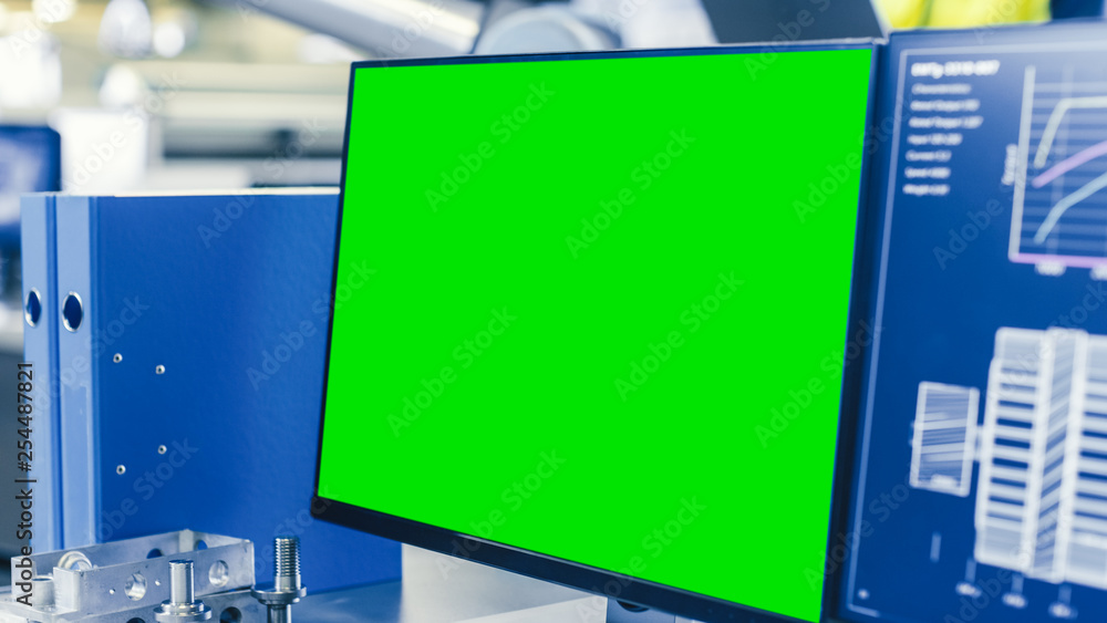 Poster Close-up Shot of the Computer Monitor with Green Screen Chroma Key Great for Mock up Template. In the Background Manufacturing Factory with People Working.