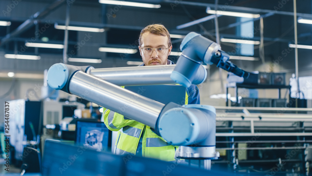 Poster At the Factory: Automation Engineer Uses Laptop for Programming Robotic Arm. New Era in Automatic Manufacturing Industry.