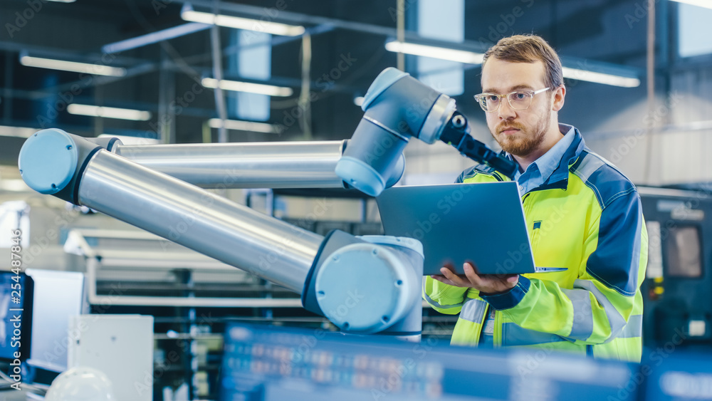 Poster At the Factory: Automation Engineer Uses Laptop for Programming Robotic Arm. New Era in Automatic Manufacturing Industry.