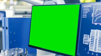 Fototapeta premium Close-up Shot of the Computer Monitor with Green Screen Chroma Key Great for Mock up Template. In the Background Manufacturing Factory with People Working.