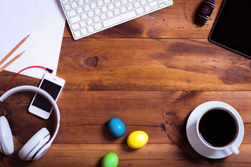 Business work desk with devices and happy easter holiday multicolored eggs background on decorated...