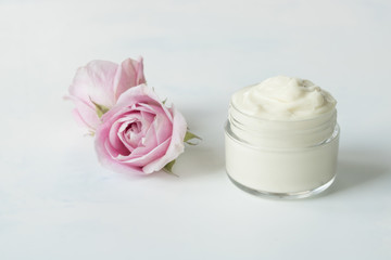 Natural face and body cream in a jar with a rose flower next to on a white background