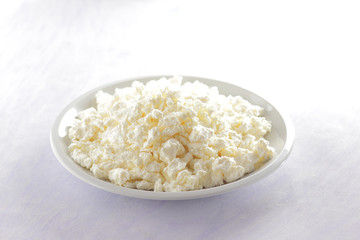 Cottage cheese on white plate with wooden spoon. Cottage cheese on white background. Soft cheese for diet. Healthy dairy product for breakfast