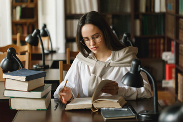 Pretty female student with books working in a high school library