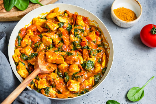 Top View On Bombay Chicken Curry With Spinach, Tomato And Onion In A White Frying Pan On A Kitchen Table. Indian Traditional Cuisine.