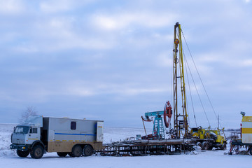 Wireline equipment hanging from top drive ready to be lowered downhole for logging. An oil well engineer works from the back of specialised van to log the condition of steel casing inside an oil well
