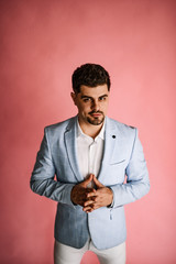 A handsome man in light jeans and a blue jacket posing on a pink background. Men's business photo shoot in the Studio.
