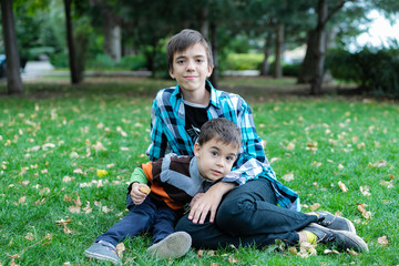 Naklejka na ściany i meble Brothers Hugging. Two boys outside in a field back lit with rays of sunshine, cuddling. Telling secrets, giggling, laughing, sibling love. Outdoor creamy, bright, portrait of kids sitting together.