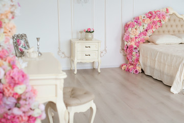 Bedroom in soft light colors. Big comfortable double bed decorated with flowers in elegant classic...