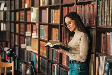 Brunette female student with book in hands in a bookspace