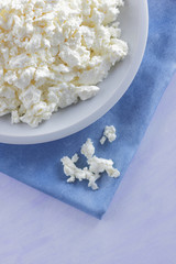 Cottage cheese on blue napkin. Cottage cheese on white plate with wooden spoon. Soft cheese for diet. Healthy dairy product for breakfast