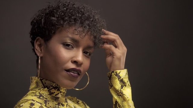 mixed race african american woman in bright yellow dress with python print. 90's style touches her natural curly short hair and smiling to the camera. Studio shoot black background