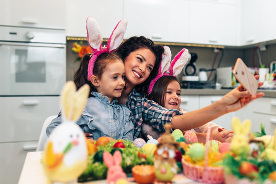 A mother and her cute daughters are taking selfie photo while painting eggs. Happy family are preparing for Easter.