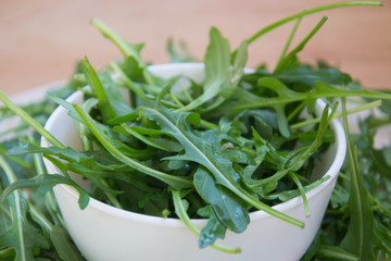 Green arugula leaves on wooden cutting board. Fresh rucola in the kitchen in porcelain bowl,...