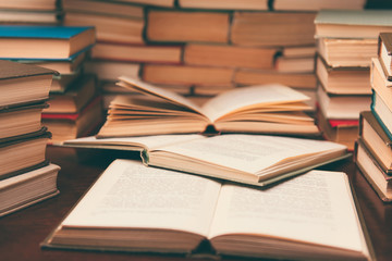 Old book in library with open textbook, stack piles of literature text archive on reading desk in school study class room background for education learning concept. Narrow depth of field