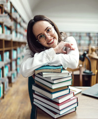 Portrait of brunette teenage girl holding books near the table at the library