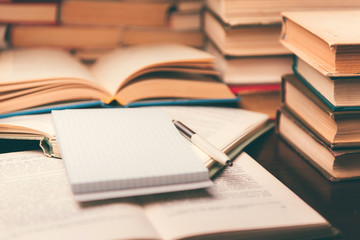 Education learning concept with open book and notebook on the table. Stack piles of books on reading desk and glasses in bookshelves background