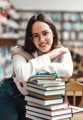 Girl standing with hands folded on books in library