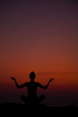 Fototapeta premium Yoga near the sea at sunset. Meditation and relaxation. Siluet.